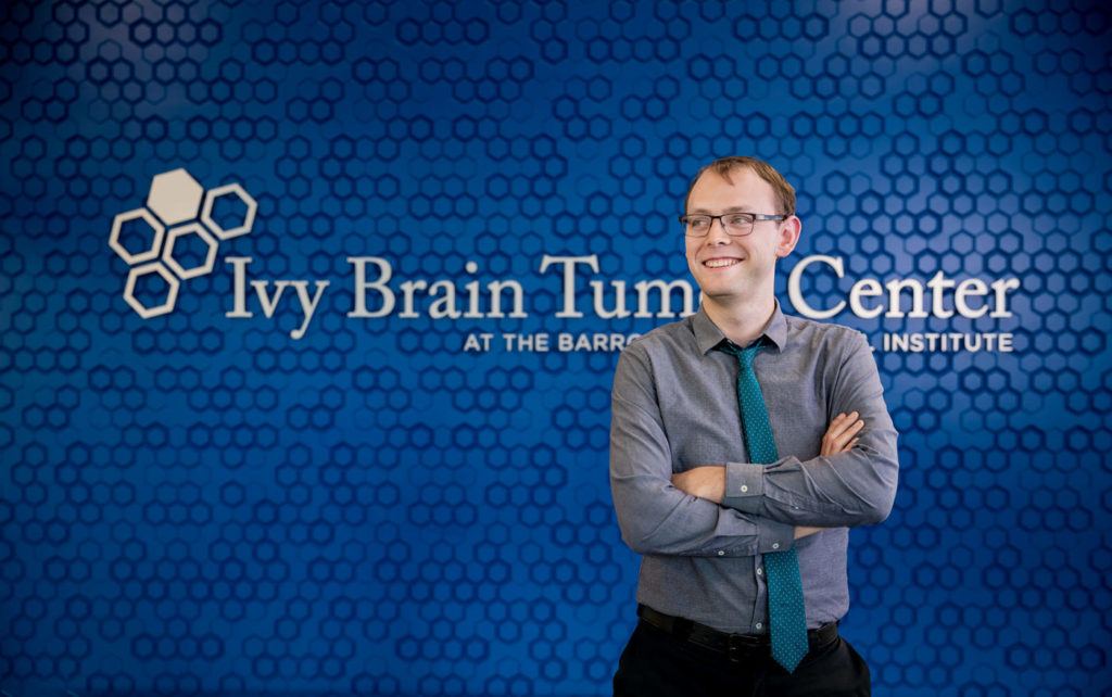 Ivy patient, Nick Stump, standing in front of Brain Tumor Center wall