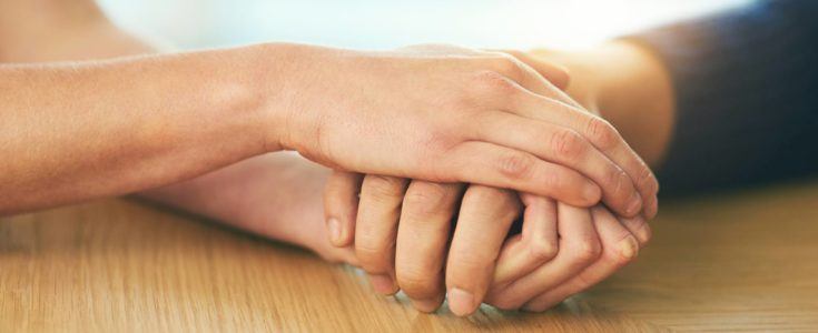 Person with their hand clasped between both hands of another person