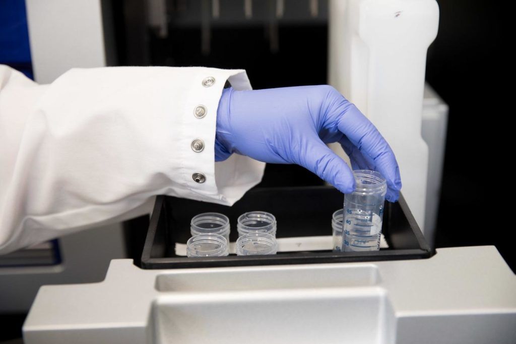 Gloved hand putting tubes of liquid into a container