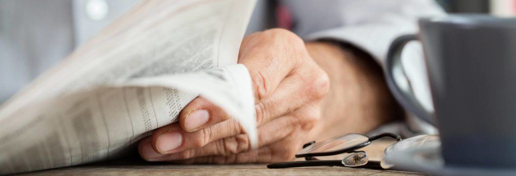 Hand holding the newspaper resting on a table with a cup of coffee