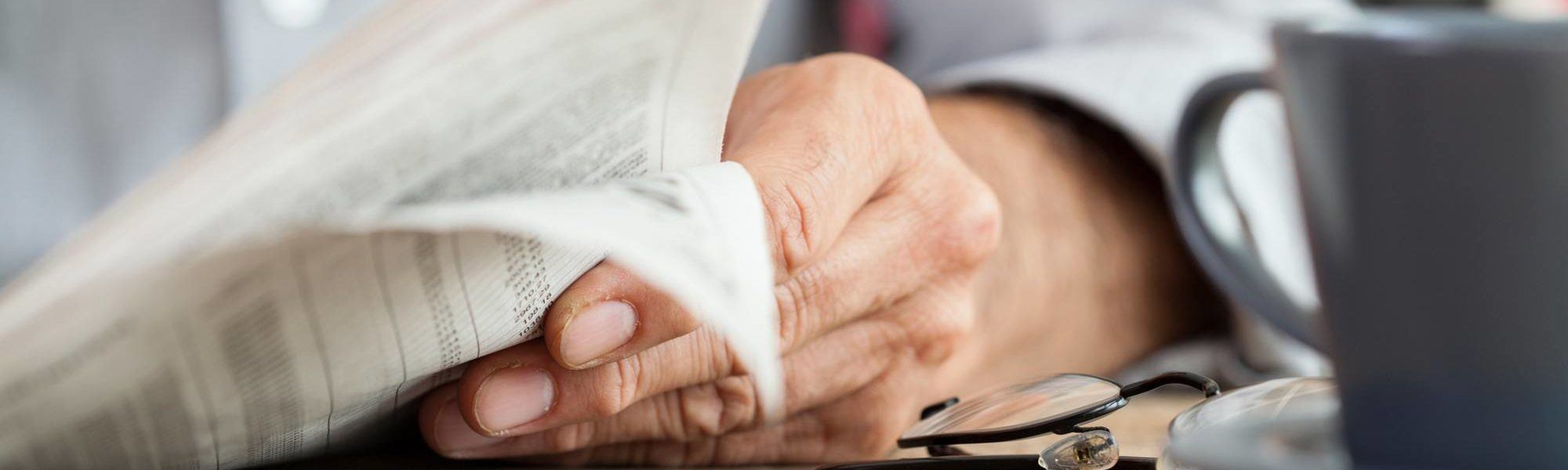 Hand holding the newspaper resting on a table with a cup of coffee