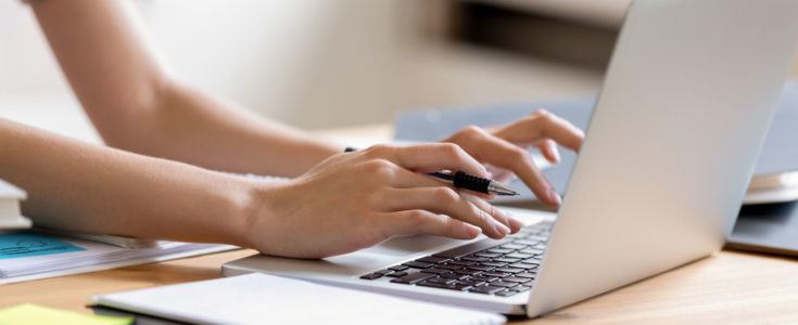 Woman hands holding pen and typing on computer