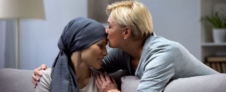 Caregiver giving cancer patient a kiss on forehead